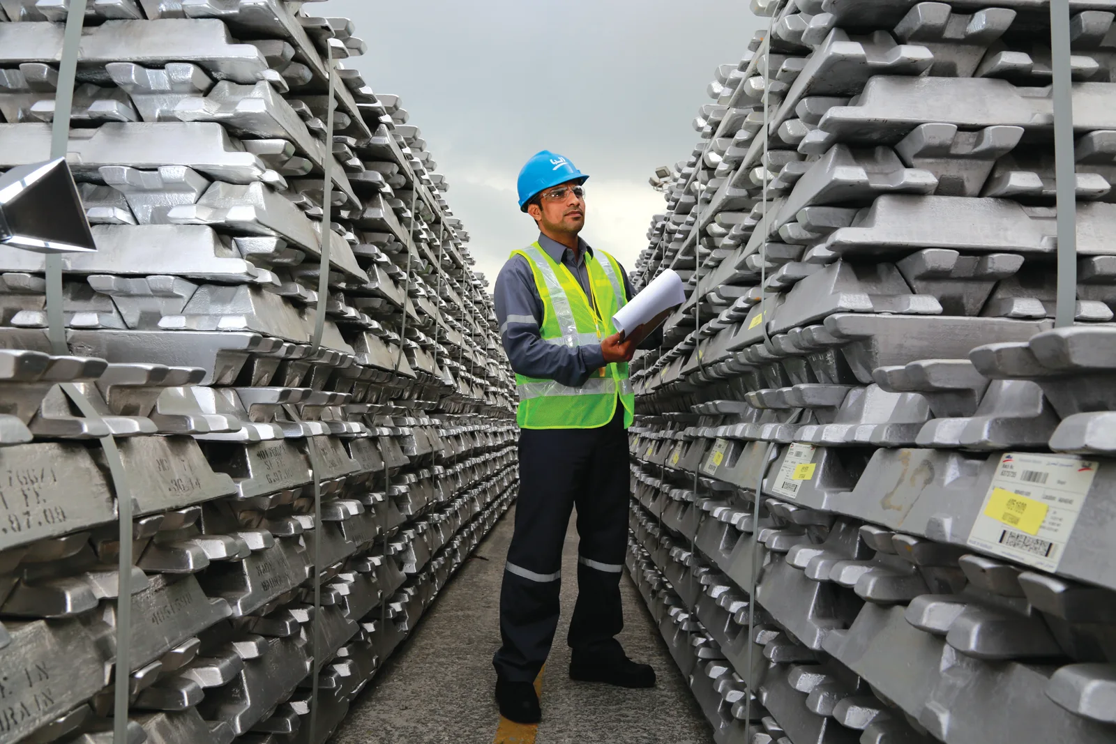 Rows of stacked aluminium ingots with an industrial worker inspecting stock